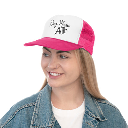 A smiling woman with blonde hair wearing a trucker hat. The hat has a white front panel with the phrase 'Dog Mom AF' in black cursive lettering and a vibrant pink mesh back.